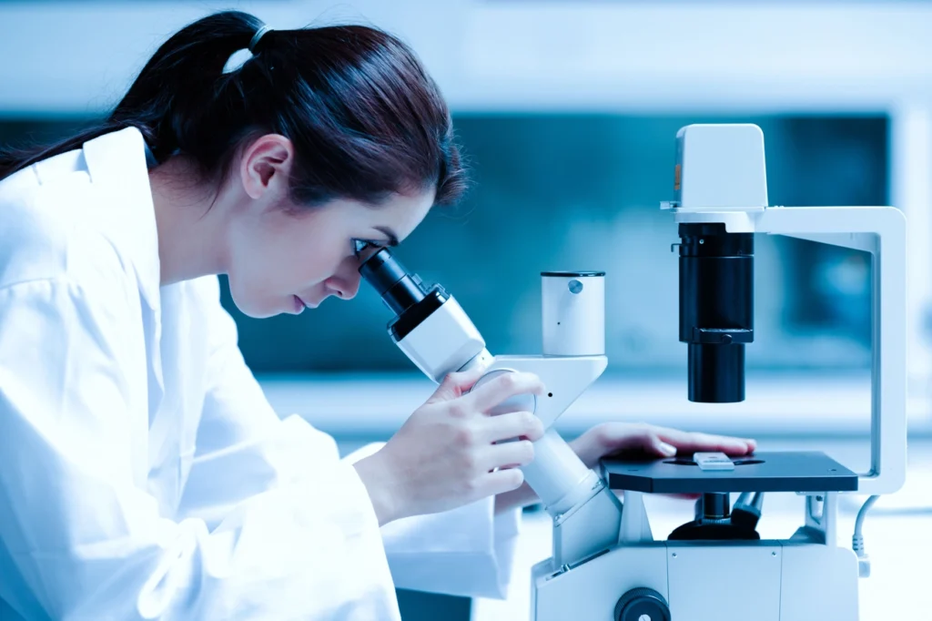 Scientist in a white lab coat examining a sample through a microscope in a medical laboratory. Hepatitis Testing